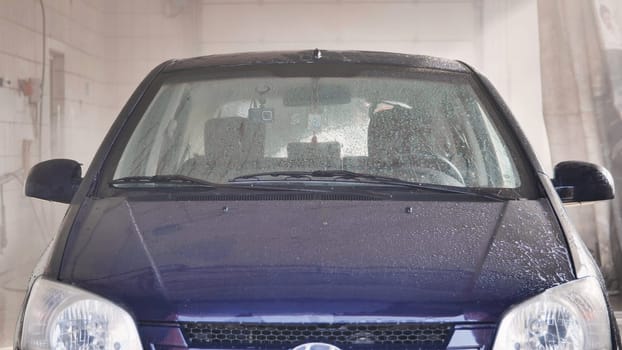 Car getting washed in automatic car wash with soap foam and water spraying on windshield