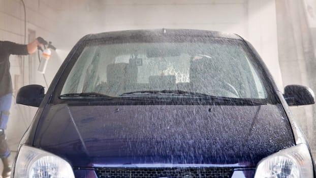 Car wash worker spraying foam on a vehicle with a high pressure water jet