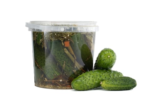 Green cucumbers placed next to a transparent plastic container filled with brine pickles.