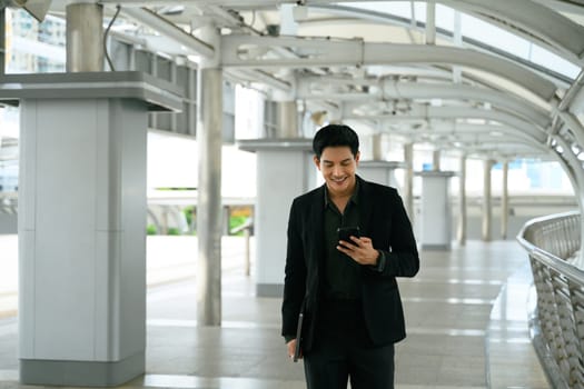 Confident businessman using smartphone walking in modern city walkway.