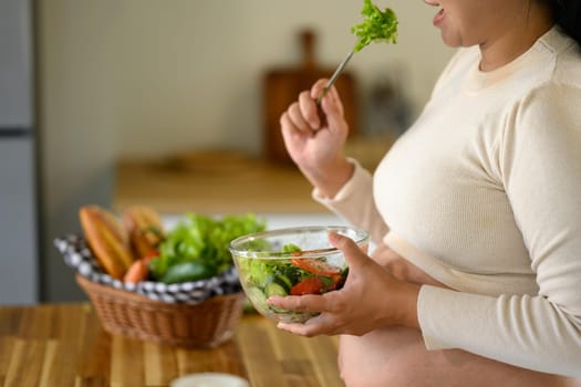 Expectant mother enjoying a vegetable salad in a kitchen, balanced diet for prenatal health.