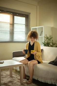 Relaxed woman enjoying her morning coffee and checking her phone in a softly lit home.