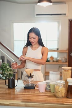 Asian woman preparing pour over coffee with fresh beans and mugs on the counter.