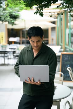 Smiling man working remotely on a laptop at a modern outdoor cafe.