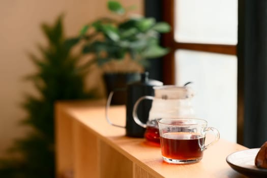A glass filled with black coffee beside a pour over carafe on a wooden table with warm morning light.