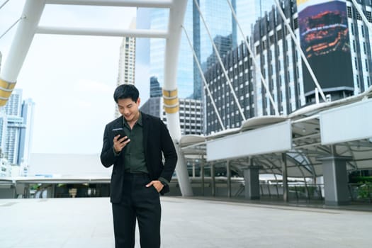 Businessman checking his smartphone while walking through a modern city district.