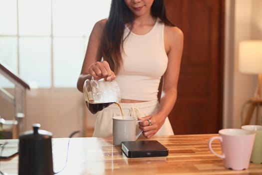 Young woman pouring freshly brewed coffee into a mug in a home kitchen.