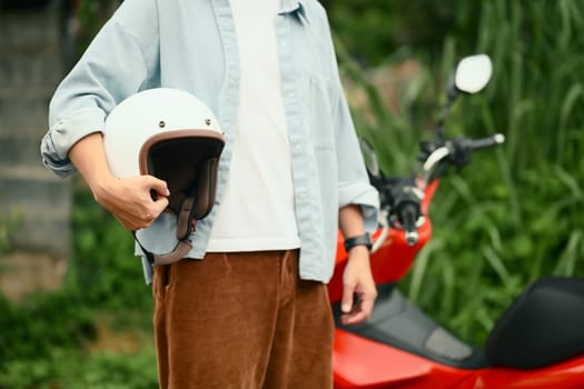 Safety and style concept with male commuter carrying his helmet next to a parked scooter.