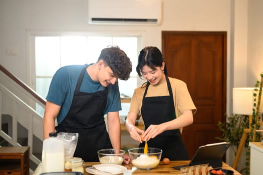 Smiling couple preparing pancake batter together in the kitchen.