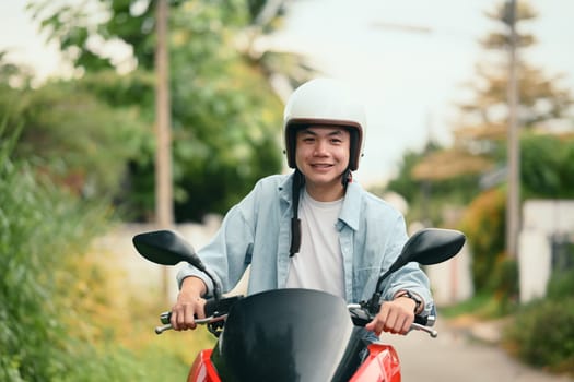 Cheerful young man wearing helmet riding a red motorcycle on a quiet residential street.