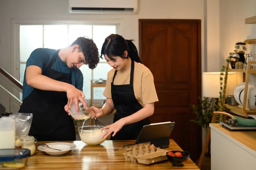 Smiling couple preparing pancake batter together in the kitchen.