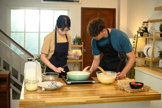 Happy young couple in aprons preparing to cook pancakes in a cozy home kitchen.
