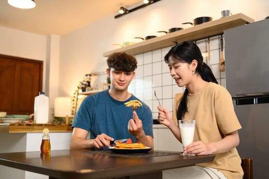 Cheerful young couple enjoying homemade pancakes together at the dining table.