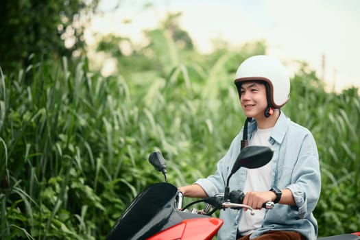 Smiling young man wearing helmet riding a red motorcycle on a quiet residential street.