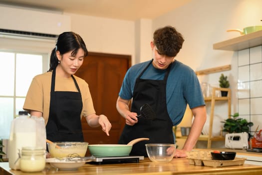 Happy young couple in aprons preparing to cook pancakes in a cozy home kitchen.