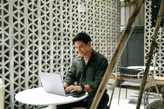 Smiling man working remotely on a laptop at a modern outdoor cafe.