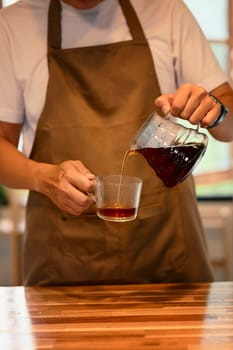 Cropped shot of man pouring fresh brewed coffee into glass cup in a kitchen.