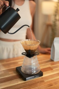 Close up of a woman pouring hot water into a pour-over coffee filter at home.