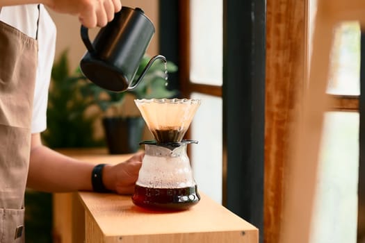 Close up of man brewing coffee with pour over method using a glass dripper in a kitchen.