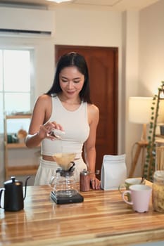 Beautiful woman pouring coffee grounds into a pour-over filter while brewing fresh coffee.