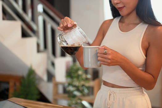 Young woman pouring freshly brewed coffee into a mug in a home kitchen.