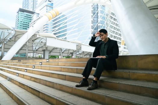 Businessman sitting on outdoor steps, looking tired and overwhelmed from work stress.