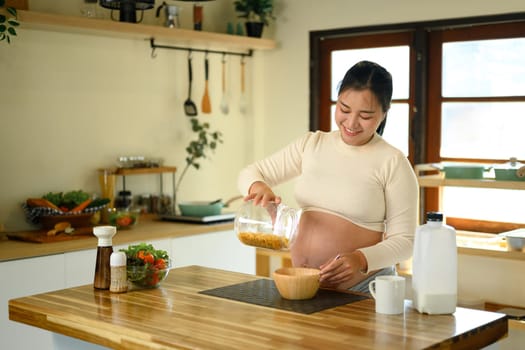 Cheerful pregnant woman preparing a simple and healthy breakfast in the kitchen.