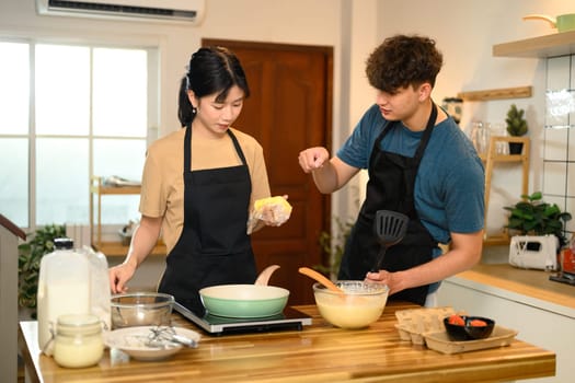 Man and woman wearing aprons preparing pancakes at home.