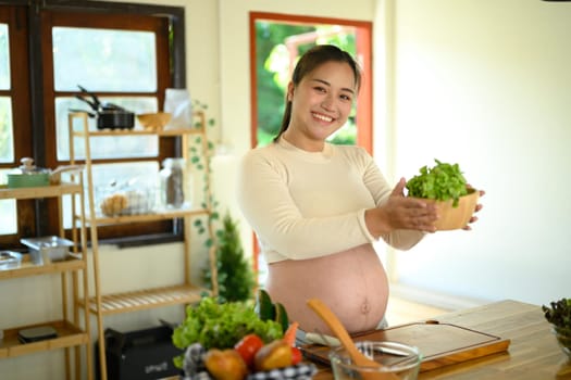 Happy pregnant woman preparing a nutritious meal with fresh ingredients in home kitchen.