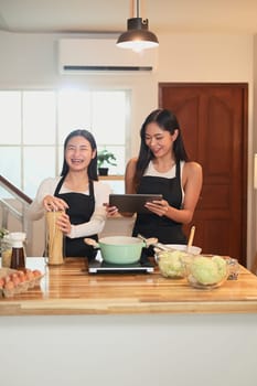 Beautiful asian mother and daughter cooking pasta together in the kitchen.