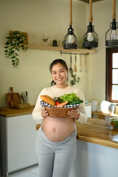 Happy pregnant woman preparing a nutritious meal with fresh ingredients in home kitchen.