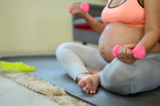 Close up of pregnant woman sitting holding pink dumbbells for a light home workout.