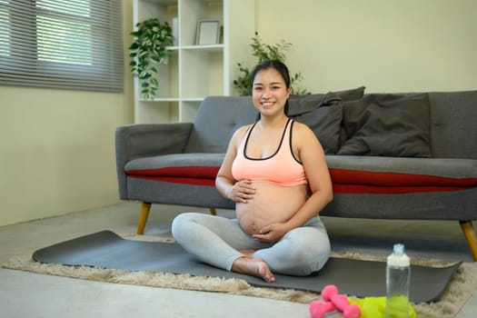 Happy pregnant woman relaxing on a mat during her home workout routine.