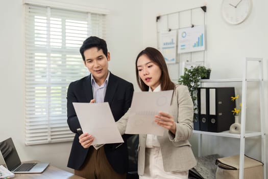 Two business professionals engage in a strategic discussion, reviewing project documents and collaborating in a contemporary office environment.