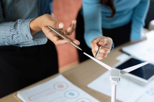Two business professionals engage in a discussion about renewable energy strategies, focusing on a wind turbine model to emphasize sustainability.