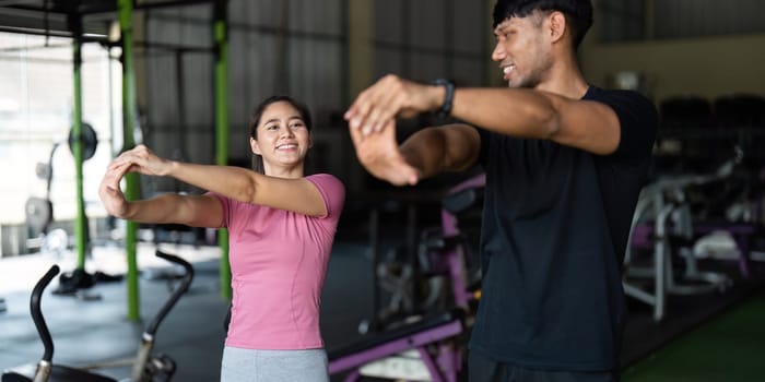 A young couple performs warm-up stretches together in a gym, promoting fitness and connection.