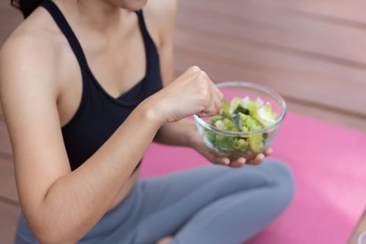 A health-conscious woman enjoys a nutritious salad on a yoga mat, highlighting the importance of healthy eating.