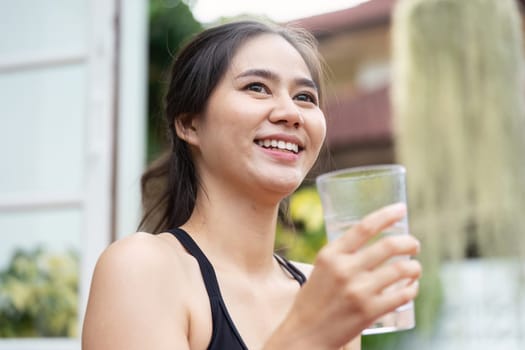 A young woman happily holds a glass of water, embodying the essence of hydration and wellness in a natural setting.
