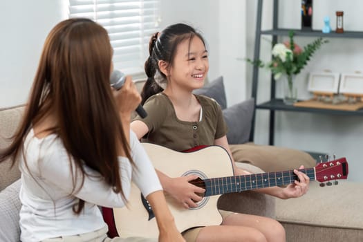 A young girl plays guitar while her mother sings, creating a warm and loving atmosphere. Perfect for family and music themes.