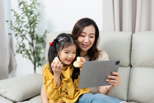 The mother and daughter share a delightful moment as they engage with a tablet, showcasing their close relationship and modern family life.