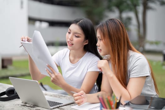 Sitting in a serene environment, two friends concentrate on their schoolwork, using their laptops and documents to collaborate effectively on assignments.
