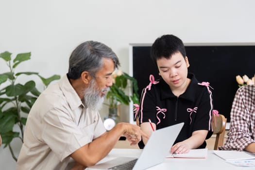 A grandfather provides guidance to a girl with Down syndrome, helping her understand her studies while her friend watches, showcasing family support.