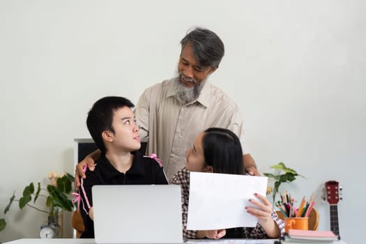 A caring grandfather supports a girl with Down syndrome and her friend as they navigate their learning materials, fostering a nurturing environment.