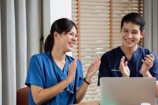 A doctor and a nurse share a joyful moment in a meeting, applauding their teamwork and discussing patient care strategies. Their camaraderie enhances their professional environment.