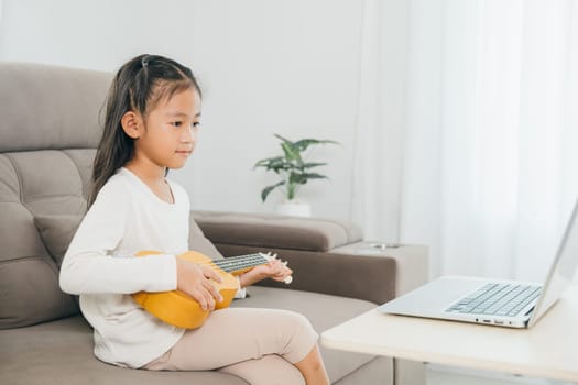 A young girl practicing ukulele on a couch, using a laptop for online tutorials. This scene illustrates the convenience and innovation of music education in a personalized, home setting.