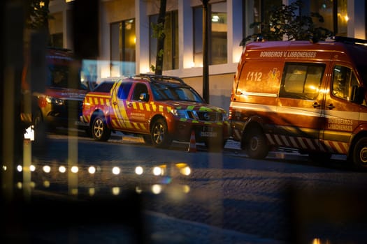 21 may 2025, Lisbon, Portugal - Fire trucks parked on a city street at night, reflecting in a window, creating a sense of urgency and preparedness
