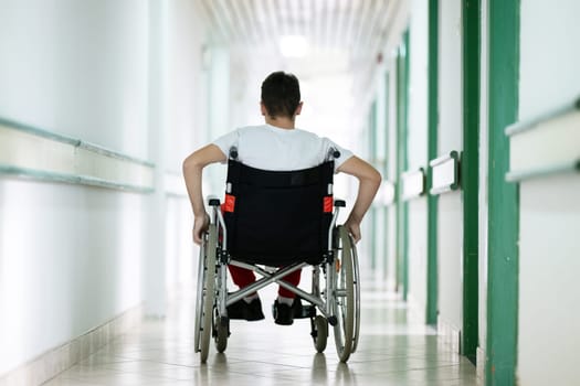Young teenage boy smiling while sitting in a wheelchair in a hospital hallway. Rehabilitation and positivity concept