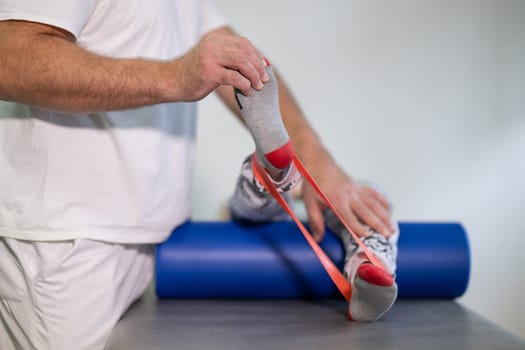 Therapist assisting with leg stretching using a resistance band during physical rehabilitation therapy session.
