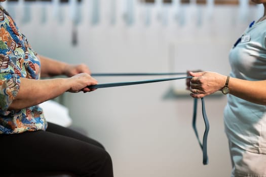 Senior woman doing physical exercises with the help of a smiling therapist. Concept of elderly rehabilitation and movement recovery.