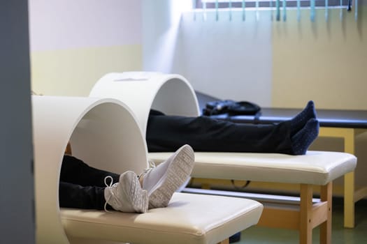 Patients lying down with legs inside circular magnetic therapy devices during a physiotherapy session.